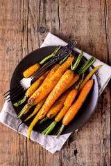 Baked Roasted Raw Freah Carrots with Olive Oil and Spices Lying on Plate Top View Horizontal Healthy Diet Organic Food Wooden Background Copy Space