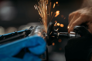 Worker cutting, grinding and polishing motorcycle metal part with sparks indoor workshop, close-up.