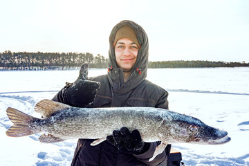 young man holding fish catch a big pike ice fishing