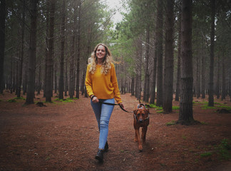 Young blonde woman walking with her dog in forest