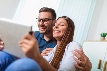 Young couple watching media content online in a tablet in the living room.