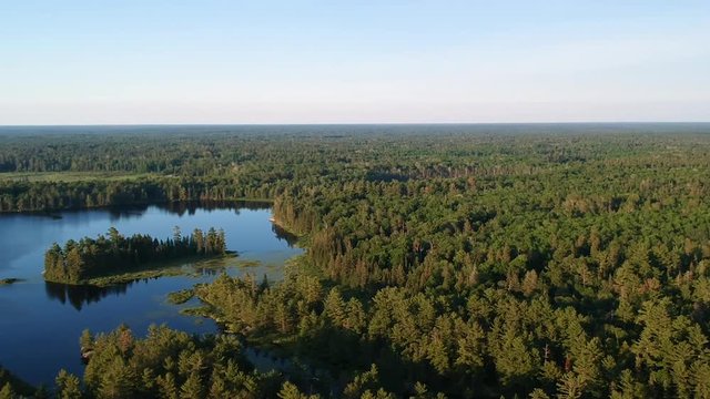 Aerial shot panning over endless evergreen pine coniferous boreal forest going behind horizon and lake with still calm blue water reflecting pine trees.
Grundy lake, Northern Ontario, Canada