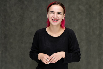 Portrait to the waist of a pretty girl with red hair on a gray background in a black jacket. Standing right in front of the camera in a studio with emotions, talking, showing hands, smiling