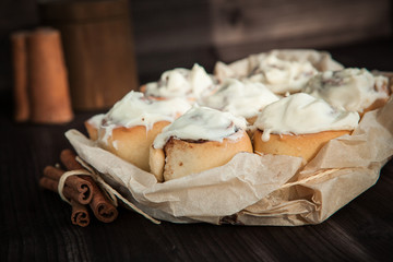 fresh cinnamon rolls and cream on a wooden background, cinnamon sticks