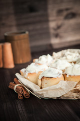 Fototapeta na wymiar fresh cinnamon rolls and cream on a wooden background, cinnamon sticks