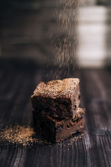 brownie cake sprinkled with ground cocoa on a dark background