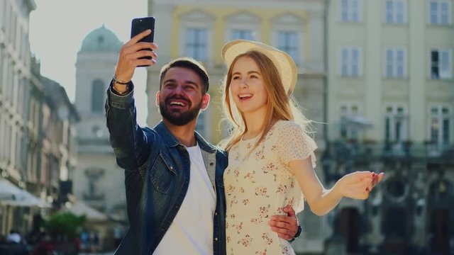 Romantic wonderful young people in trendy clothes making selfie near city modern buildings