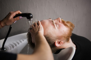 girl barber washes the hair of a young man in the barbershop