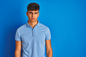 Young indian man wearing casual polo standing over isolated blue background skeptic and nervous, frowning upset because of problem. Negative person.