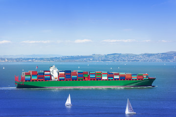 Full loaded cargo ship in sea among white yachts