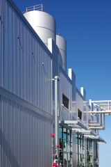 Perspective view of a modern industrial building with silos in the back under a deep blue sky