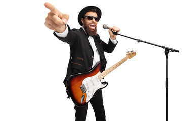 Man with an electric guitar singing on a microphone and pointing