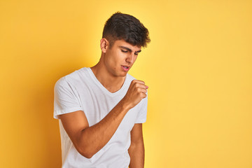 Young indian man wearing white t-shirt standing over isolated yellow background feeling unwell and coughing as symptom for cold or bronchitis. Healthcare concept.