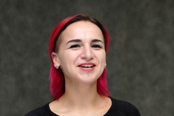 Close-up Portrait of the shoulders of a pretty girl with red hair on a gray background in a black jacket. Standing directly in front of the camera in the studio with emotions, talking, smiling.