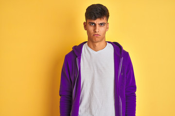 Young indian man wearing purple sweatshirt standing over isolated yellow background skeptic and nervous, frowning upset because of problem. Negative person.