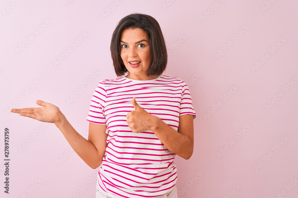 Wall mural young beautiful woman wearing striped t-shirt standing over isolated pink background showing palm ha