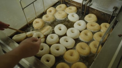 Baker flipping donuts floating in bubbling hot oil in fryer / Pleasant Grove, Utah, United States - Powered by Adobe