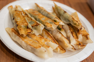 The various flavor of Pan-fried dumplings or gyoza in a paper plate placed on a wooden table.