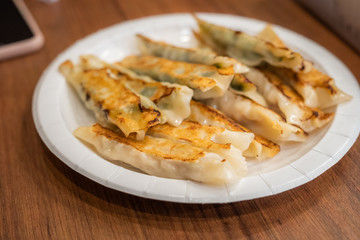 The various flavor of Pan-fried dumplings or gyoza in a paper plate placed on a wooden table.