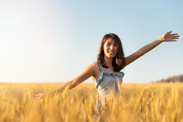 Beautiful and happy asian woman enjoying life in barley field at sunset.