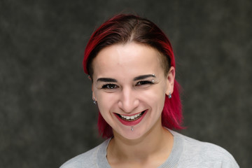 Close-up portrait on the shoulders of a pretty girl with red hair on a gray background in a gray jacket. Standing directly in front of the camera in the studio with emotions, talking, smiling.