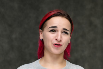 Close-up portrait on the shoulders of a pretty girl with red hair on a gray background in a gray jacket. Standing directly in front of the camera in the studio with emotions, talking, smiling.