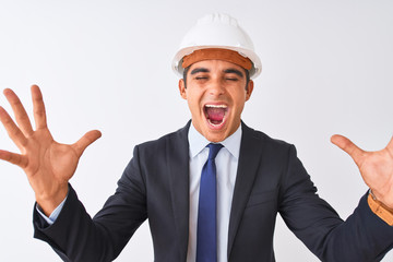 Young handsome architect man wearing suit and helmet over isolated white background celebrating mad and crazy for success with arms raised and closed eyes screaming excited. Winner concept