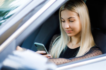 Fototapeta na wymiar Beautiful woman smiling while sitting on the front seats in the car. Girl is using a smartphone
