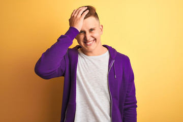 Young handsome man wearing purple sweatshirt standing over isolated yellow background surprised...