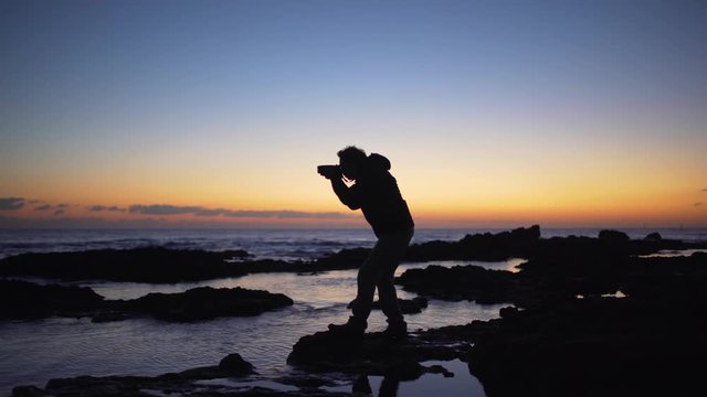 A photographer silhouette taking photos in the sea at sunset	