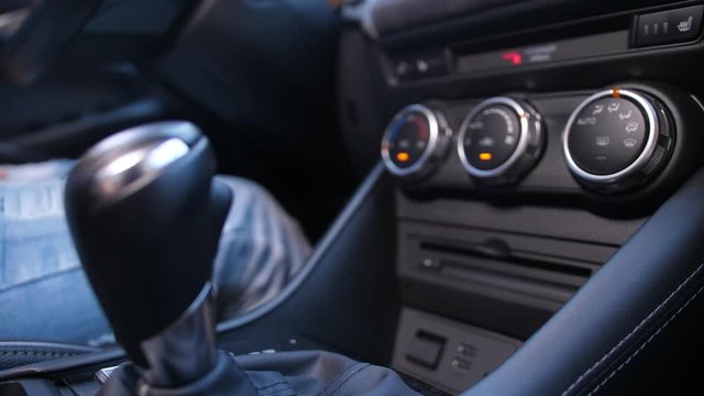 Close-up of female driver hand switching automatic transmission in luxury car before driving. Black leather car interior view, woman sitting on driver's seat shifting gear knob going to drive car