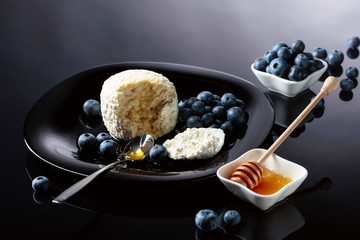 Cottage cheese with honey and blueberry on a black plate.