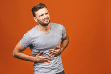 Man in pain holding his hurting stomach isolated on the orange background. Abdominal pain.