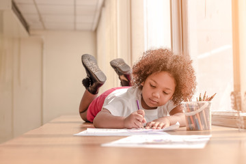 Little toddler girl laying down concentrate on drawing.  Mix African girl learn and play in the pre-school class. Children enjoy hand writing. 3 years girl enjoy playing at nursery.