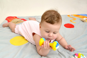 The small child looks at a rattle, lying on a stomach