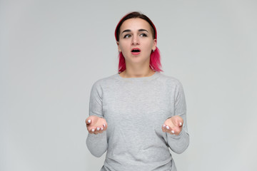 Portrait to the waist of a pretty girl with red hair on a white background in a gray sweater. Standing right in front of the camera in a studio with emotions, talking, showing hands, smiling