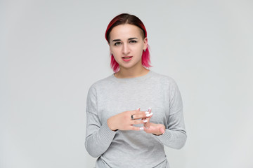 Portrait to the waist of a pretty girl with red hair on a white background in a gray sweater. Standing right in front of the camera in a studio with emotions, talking, showing hands, smiling