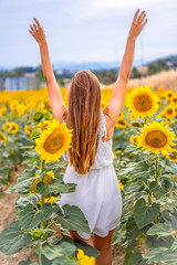 Lifestyle session. A young Caucasian blonde with short dress among sunflowers with raised arms