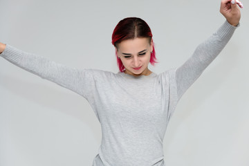 Portrait to the waist of a pretty girl with red hair on a white background in a gray sweater. Standing right in front of the camera in a studio with emotions, talking, showing hands, smiling