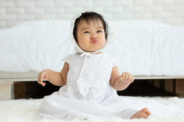 Cute Sweet Adorable Asian Baby wearing white dress sitting on Carpet smiling and playing with happiness emotional in cozy bedroom,Healthy Baby Concept