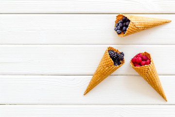 Summer breakfast with fresh berries in waffle cones on white wooden background top view mockup