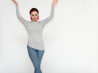 Portrait of a knee-high pretty girl with red hair on a white background in a gray sweater and blue jeans. Standing right in front of the camera with emotions, talking, showing hands, smiling