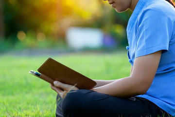 Portrait of beautiful young women who relax by watching the tablet in the lawn relax. Smiling Thai woman using digital tablet while lying in green spring garden