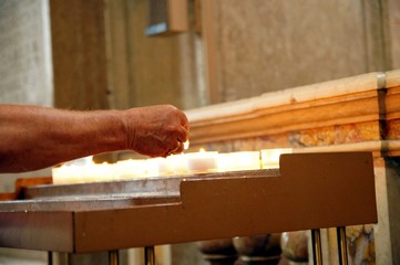 Woman holding candle near altar in church. old woman's hand lighting candles in a cathedral. lighting prayer candle offering, sacrificial or memorial candles lit in a church.