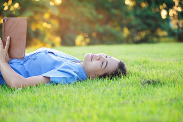 Portrait of beautiful young women who relax by watching the tablet in the lawn relax. Smiling Thai woman using digital tablet while lying in green spring garden