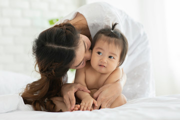 Happy Beauty mother Hugging and kissing Cute Sweet Adorable Asian Baby wearing white dress sitting on Carpet smiling and playing with happiness emotional in cozy bedroom,Healthy Baby Concept