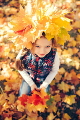 Naklejka na ściany i meble Portrait of smiling child with wreath of leaves on head and a bouquet of leaves in the hands. Background of sunny autumn park.