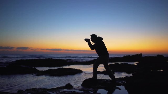 A photographer silhouette taking photos in the sea at sunset	