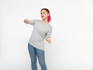 Portrait of a knee-high pretty girl with red hair on a white background in a gray sweater and blue jeans. Standing right in front of the camera with emotions, talking, showing hands, smiling