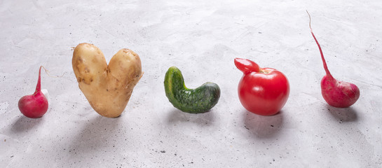 Five ugly vegetables are standing in row on grey concrete background. 